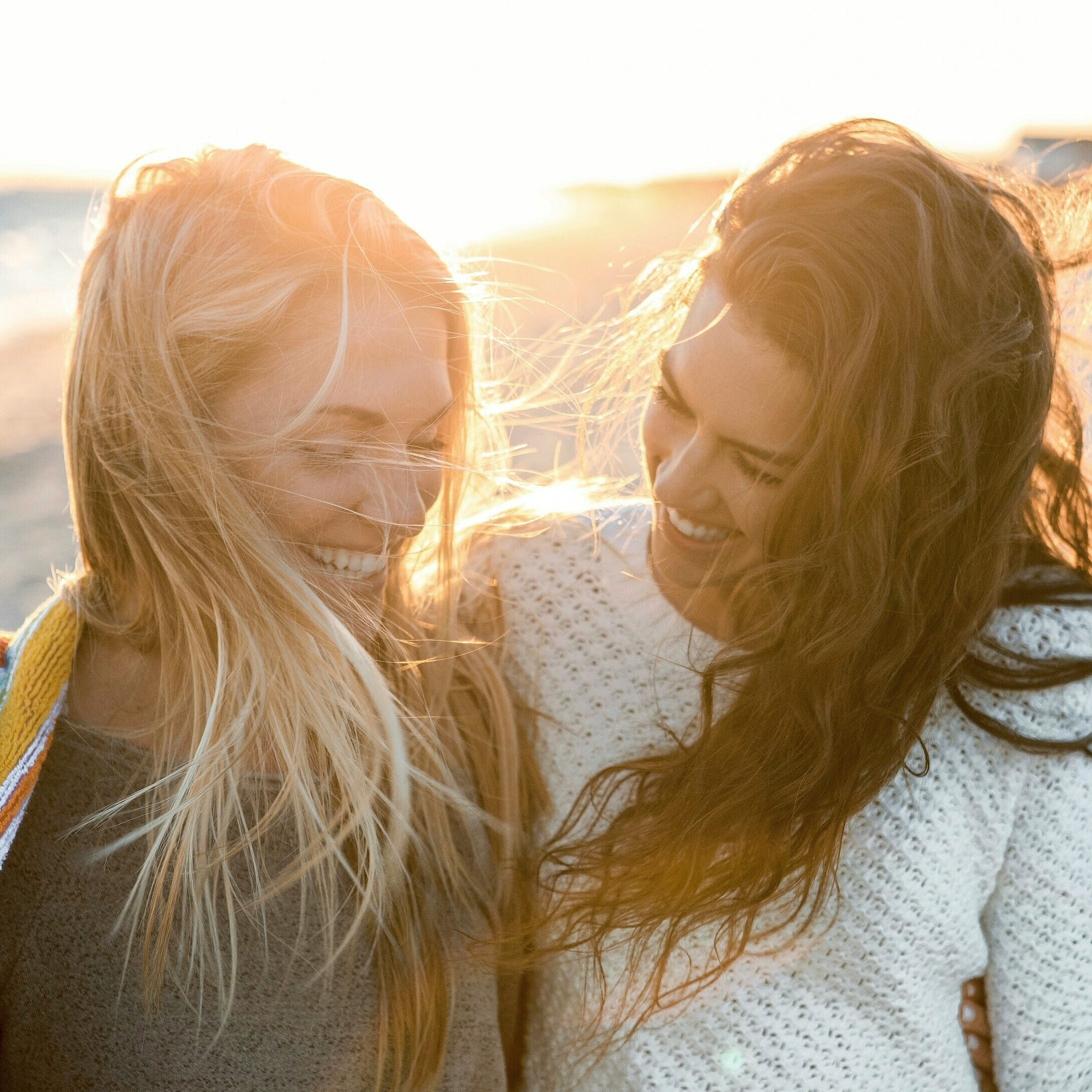 Two women smiling at each other, with sunlight and wind creating a joyful atmosphere.