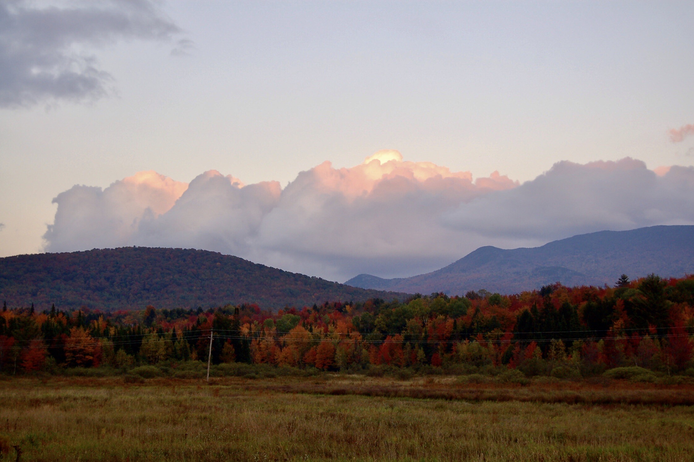 Vibrant autumn foliage with mountains and clouds at sunset.