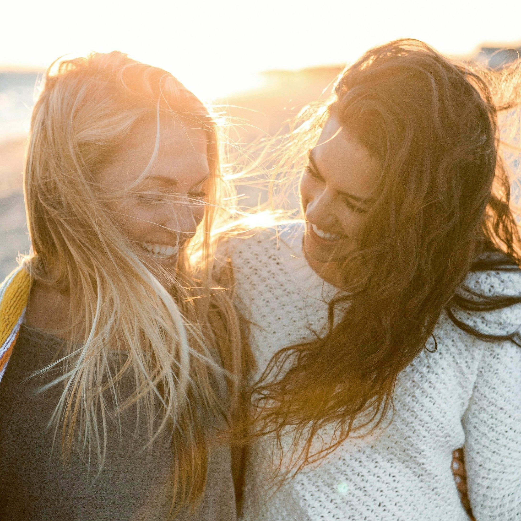 Two women laughing and enjoying each other's company at sunset, with windswept hair.