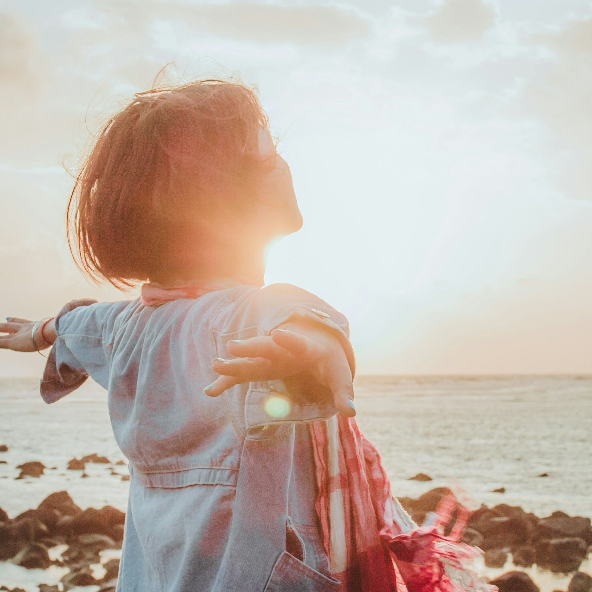 Person with outstretched arms faces the sunset at a beach.